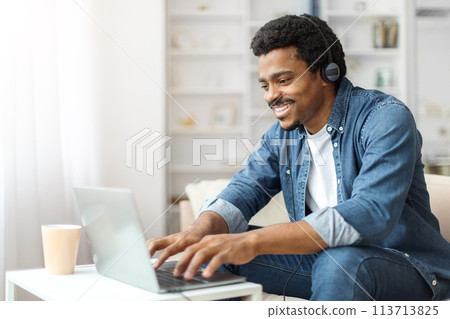 Young Black Man With Headphones Working on Laptop Indoors 113713825