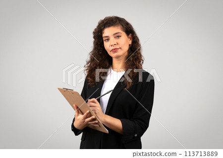 Businesswoman with clipboard looking thoughtful 113713889