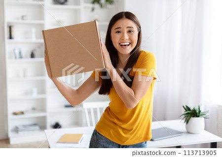 Ecstatic asian woman holding up cardboard box with joyful expression Ecstatic asian woman holding up cardboard box with joyful expression 113713905