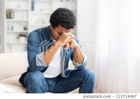 Distressed Young Black Man Seated on Couch With Hands Covering Face Distressed Young Black Man Seated on Couch With Hands Covering Face 113714067