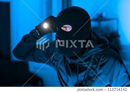 Balaclava-wearing person shining a flashlight in dark room Balaclava-wearing person shining a flashlight in dark room 113714142