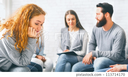 Upset redhead woman sitting at group therapy session 113714170
