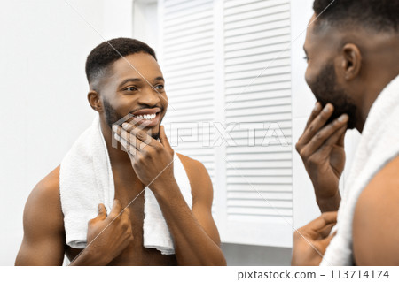 Man with towel patting face in bathroom mirror 113714174