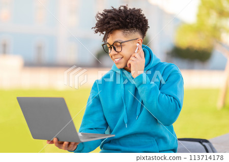 Man using phone and laptop simultaneously, studying at park 113714178