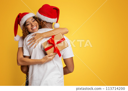 Black millennial couple with Christmas gift on orange background Black millennial couple with Christmas gift on orange background 113714200