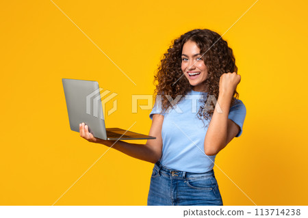 Laptop-holding woman celebrates a victory on yellow 113714238