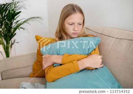 Young Girl Looking Downcast While Hugging Pillow on Couch Young Girl Looking Downcast While Hugging Pillow on Couch 113714352