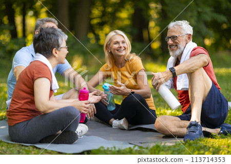Joyful senior yoga enthusiasts enjoying friendly chat while sitting on mats outdoors Joyful senior yoga enthusiasts enjoying friendly chat while sitting on mats outdoors 113714353
