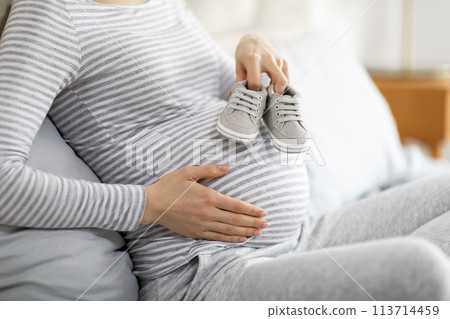 Expectant mother caressing bump with shoes, cropped 113714459