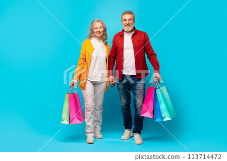 Smiling senior couple enjoys shopping carries Black Friday purchases, studio 113714472