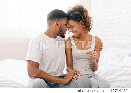 Happy couple holding positive pregnancy test on bed Happy couple holding positive pregnancy test on bed 113714481