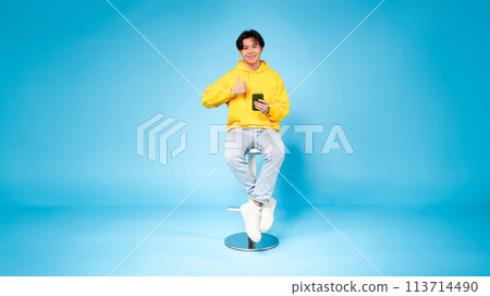 Cheerful young guy with phone gives thumbs up 113714490