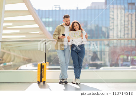 Loving couple holding map and using phone at airport Loving couple holding map and using phone at airport 113714518