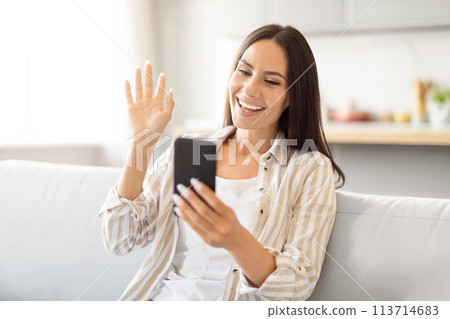 Woman video calling and waving at smartphone screen Woman video calling and waving at smartphone screen 113714683
