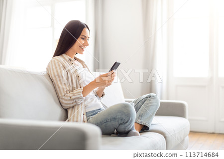 Smiling woman holding phone on sofa at home 113714684