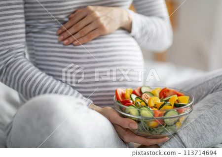 Pregnant woman eating healthy salad at home, cropped 113714694