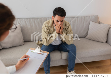 Upset man hiding face during therapy, feeling down 113714705