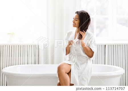 Woman sitting by a bathtub grooming herself Woman sitting by a bathtub grooming herself 113714707