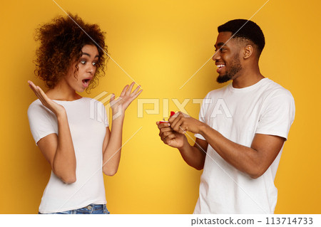 Shocked african woman looking at her boyfriend with engagement ring 113714733