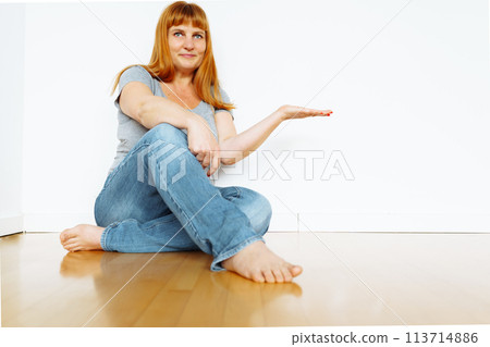 Full length portrait gorgeous cheerful woman sitting on parquet floor, empty space an apartment without furniture Full length portrait gorgeous cheerful woman sitting on parquet floor, empty space an apartment without furniture 113714886