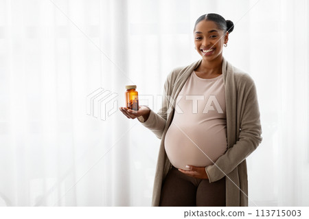 Cheerful pregnant young black woman holding jar with pills 113715003