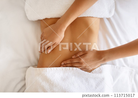Unrecognizable young woman receiving massage therapy for abdominal area indoor 113715017