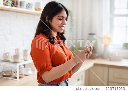 Happy woman texting on smartphone at kicthen Happy woman texting on smartphone at kicthen 113715033