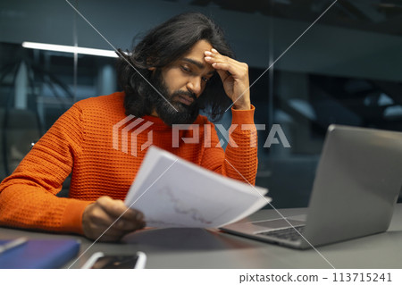 Man with headache over paperwork 113715241