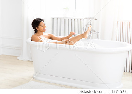 Woman relaxing in a bubble bath, shaving legs 113715283