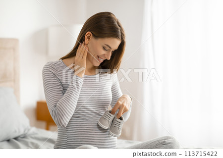 Pregnant woman touching her neck, holding baby shoes 113715422