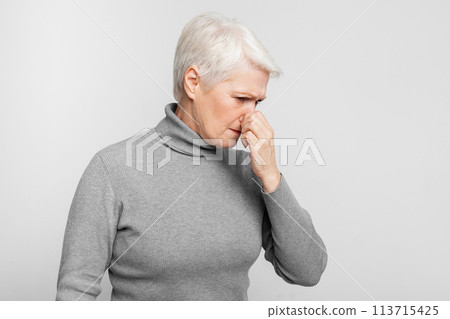 Senior woman standing with nose closed on grey background 113715425