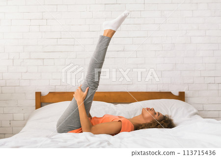 Woman doing yoga exercise on bed at home 113715436