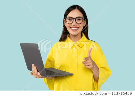 Cheerful young woman in yellow shirt holding laptop, pointing finger to camera and smiling, choosing you Cheerful young woman in yellow shirt holding laptop, pointing finger to camera and smiling, choosing you 113715439