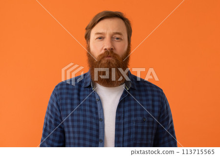 Redhaired man looking at camera with calm expression, orange background 113715565