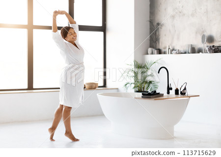 Beautiful Black Female In White Bathrobe Relaxing And Stretching In Modern Bathroom Beautiful Black Female In White Bathrobe Relaxing And Stretching In Modern Bathroom 113715629