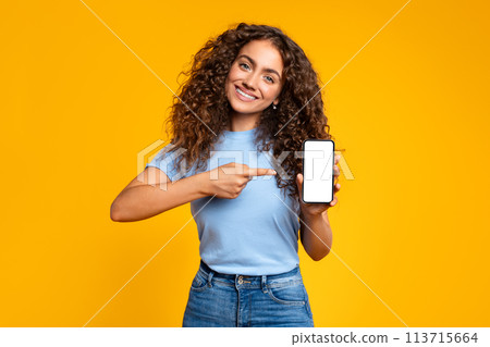 Cheerful woman pointing at smartphone screen on yellow Cheerful woman pointing at smartphone screen on yellow 113715664