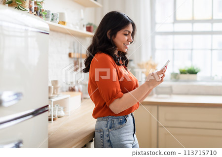 Woman browsing phone in a cozy kitchen 113715710
