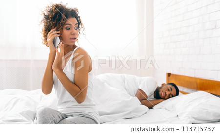 Woman on phone with man asleep in bed Woman on phone with man asleep in bed 113715737