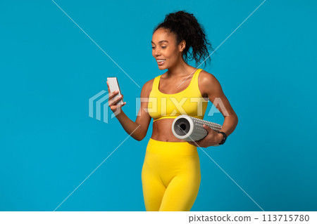 Woman checking phone holding a yoga mat Woman checking phone holding a yoga mat 113715780