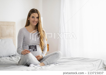 Pregnant lady holding ultrasound image at home Pregnant lady holding ultrasound image at home 113715837