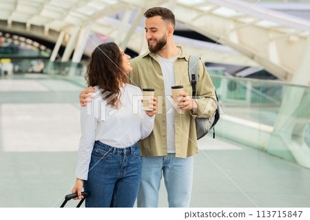 Happy Couple Walking Through an Airport With Takeaway Coffee Happy Couple Walking Through an Airport With Takeaway Coffee 113715847