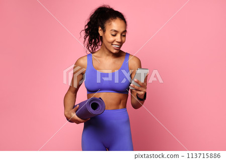 Athlete with yoga mat using phone on pink Athlete with yoga mat using phone on pink 113715886