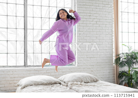 Joyful woman jumping on bed at home Joyful woman jumping on bed at home 113715941