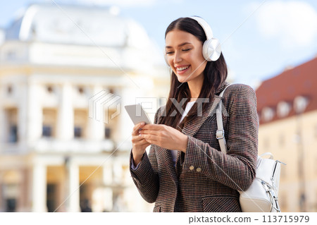 Smiling woman using phone with headphones, copy space 113715979