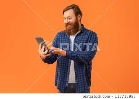Redhaired bearded man websurfing on digital tablet on orange background Redhaired bearded man websurfing on digital tablet on orange background 113715983