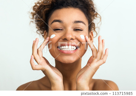 Happy lady applying facial cream on her cheeks Happy lady applying facial cream on her cheeks 113715985