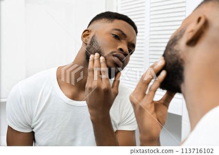 Man touching face examining skin in mirror in bathroom 113716102