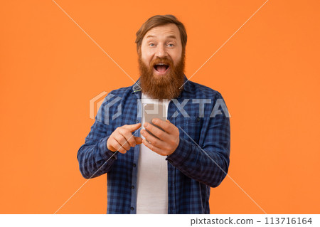 Red haired businessman expresses surprise using app on smartphone, studio Red haired businessman expresses surprise using app on smartphone, studio 113716164