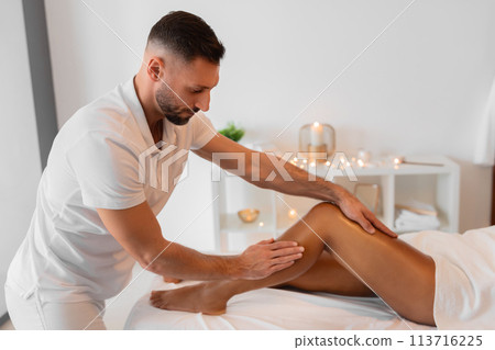 Masseur applying pressure to African American woman's leg 113716225
