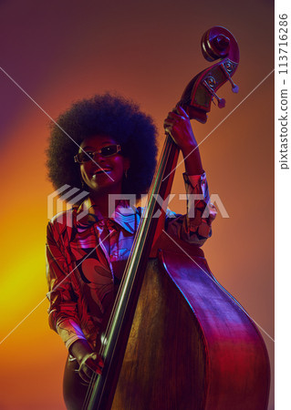 Retro-futuristic. African-American female musician in floral shirt with bass in neon light against gradient background. Retro-futuristic. African-American female musician in floral shirt with bass in neon light against gradient background. 113716286